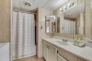 Full bath featuring vanity, wood walls, light tile patterned floors, washer / dryer, and shower / tub combo with curtain