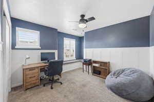 Home office featuring a wainscoted wall, a decorative wall, ceiling fan, carpet, and a textured ceiling