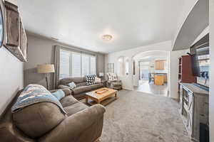Living area with arched walkways, light colored carpet, and a textured ceiling
