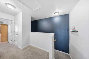 Hall featuring an upstairs landing, light colored carpet, and a textured ceiling