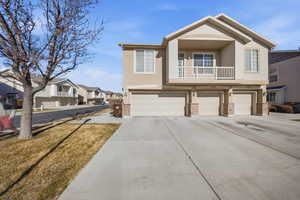 View of front facade featuring an attached garage, a balcony, brick siding, and stucco siding