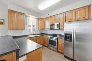 Kitchen featuring stainless steel appliances, dark countertops, backsplash, and light tile patterned flooring