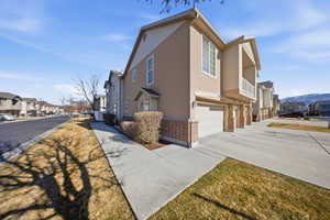 View of side of property featuring brick siding, a residential view, a garage, driveway, and stucco siding