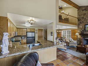 Kitchen featuring rustic walls, a chandelier, a peninsula, stainless steel appliances, and a stone fireplace