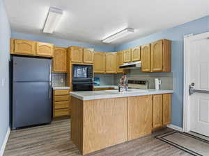 Kitchen featuring black appliances, a peninsula, tile counters, decorative backsplash, and wood finished floors