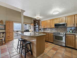 Kitchen featuring a kitchen breakfast bar, stainless steel appliances, a peninsula, tasteful backsplash, and a textured ceiling