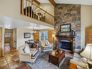 Living room featuring a fireplace, vaulted ceiling with beams, a chandelier, and log walls