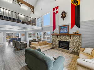 Living area featuring a ceiling fan, hardwood / wood-style flooring, a stone fireplace, wood walls, and vaulted ceiling