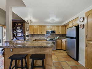 Kitchen with a peninsula, tile countertops, a kitchen bar, stainless steel appliances, and a textured ceiling