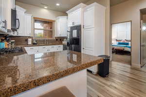Kitchen with white cabinets, light wood-style floors, black appliances, a peninsula, and backsplash