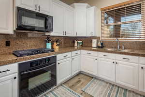 Kitchen featuring black appliances, white cabinetry, tile counters, and light wood finished floors
