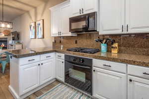 Kitchen featuring tile counters, white cabinetry, black appliances, a peninsula, and a glass covered fireplace