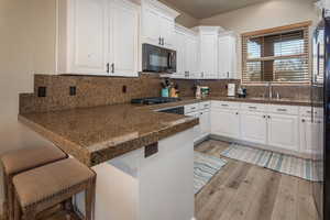 Kitchen featuring a peninsula, white cabinets, light wood-style flooring, a kitchen bar, and black appliances
