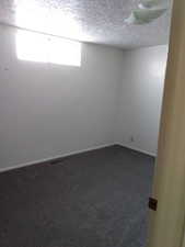 Empty room with a textured ceiling and dark colored carpet