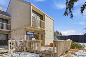Snow covered property with a balcony, stucco siding, and a deck