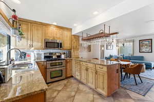 Kitchen with light stone countertops, pendant lighting, stainless steel appliances, a peninsula, and tasteful backsplash