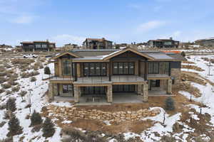 Snow covered rear of property with stone siding, a patio, a residential view, and roof mounted solar panels