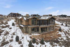 Snow covered back of property with a patio area, stone siding, and a residential view