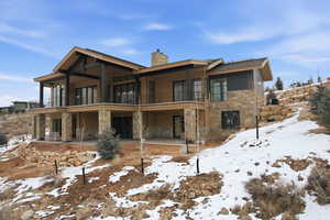Snow covered property featuring stone siding, a patio, a chimney, and a balcony