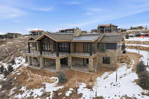 Snow covered back of property with stone siding, a patio area, a chimney, and a shingled roof