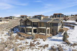 Snow covered property featuring stone siding, solar panels, and a shingled roof
