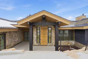 Doorway to property with stone siding, a standing seam roof, and a chimney