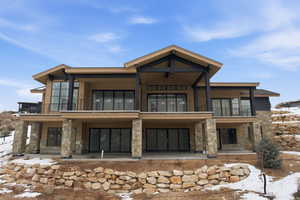 Snow covered back of property with a patio, stone siding, and a balcony