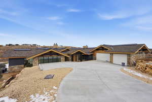 View of front of home featuring stone siding, solar panels, a chimney, and concrete driveway