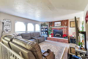 Living room with a textured ceiling, carpet, and a brick fireplace