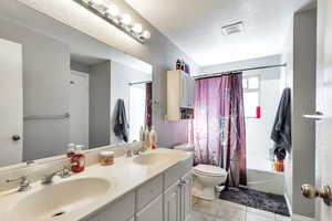 Bathroom featuring double vanity, shower / bath combo with shower curtain, light tile patterned floors, and a textured ceiling