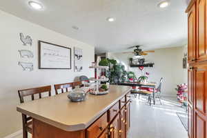 Kitchen with a kitchen island, light countertops, light flooring, wood finish cabinetry, and ceiling fan