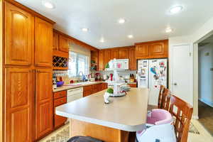 Kitchen featuring wood finish cabinets, a kitchen island, white appliances, a kitchen breakfast bar, and light countertops