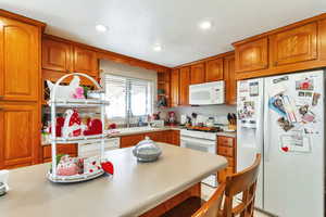 Kitchen with white appliances, wood finish cabinets, light countertops, and recessed lighting