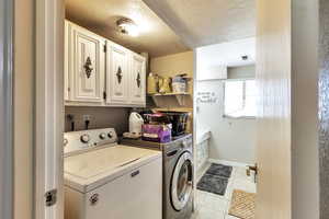 Laundry area featuring cabinet space, a textured ceiling, independent washer and dryer, and light tile patterned floors