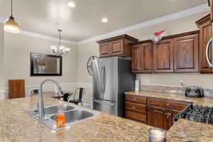 Kitchen with ornamental molding, freestanding refrigerator, suspended lighting, wainscoting, and a decorative wall