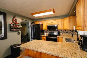 Kitchen with electric stove, freestanding refrigerator, stainless steel microwave, tasteful backsplash, and a textured ceiling