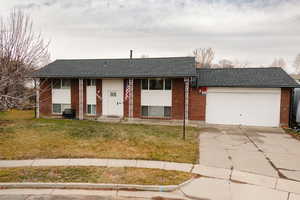 Raised ranch featuring a shingled roof, a front yard, brick siding, concrete driveway, and a porch