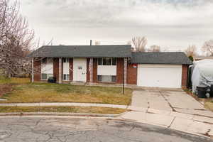 Raised ranch featuring roof with shingles, a front lawn, driveway, brick siding, and an attached garage
