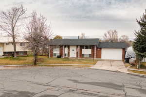 Bi-level home with brick siding, concrete driveway, a front yard, an attached garage, and a shingled roof