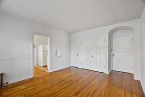 Unfurnished bedroom featuring freestanding refrigerator, light wood finished floors, radiator heating unit, and arched walkways