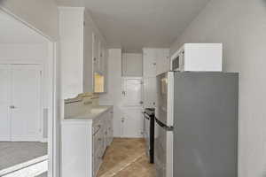 Kitchen featuring stainless steel appliances, light countertops, white cabinets, and a textured wall