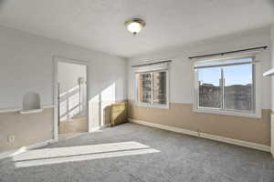 Carpeted spare room featuring radiator, a textured wall, and a textured ceiling