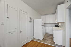 Kitchen with freestanding refrigerator, white cabinetry, light wood-type flooring, and a textured ceiling