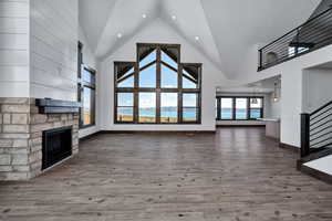 Unfurnished living room featuring a high ceiling, a stone fireplace, wood finished floors, and recessed lighting
