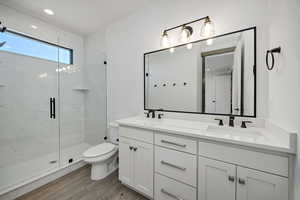 Full bath with double vanity, a marble finish shower, light wood finished floors, and recessed lighting
