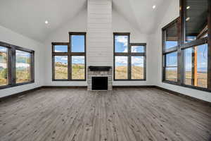 Unfurnished living room with a high ceiling, a stone fireplace, light wood-type flooring, and recessed lighting