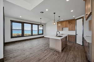 Kitchen featuring lofted ceiling, hanging light fixtures, a center island with sink, wood finish cabinetry, and light wood finished floors