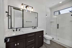 Bathroom with double vanity, a marble finish shower, recessed lighting, and light wood-style flooring