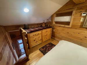 Bedroom featuring vaulted ceiling, wooden walls, and light wood finished floors