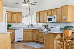 Kitchen featuring decorative light fixtures, ceiling fan, white appliances, light wood finish cabinets, and light stone counters